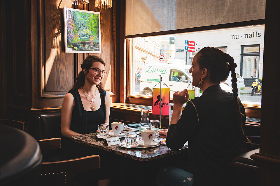 Two women sitting by a window in a Viennese coffee house laughing