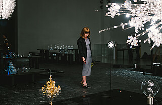 Lobmeyer: Eine Frau steht in einem dunklen Raum und um sie sind Kronleuchter aus Glas